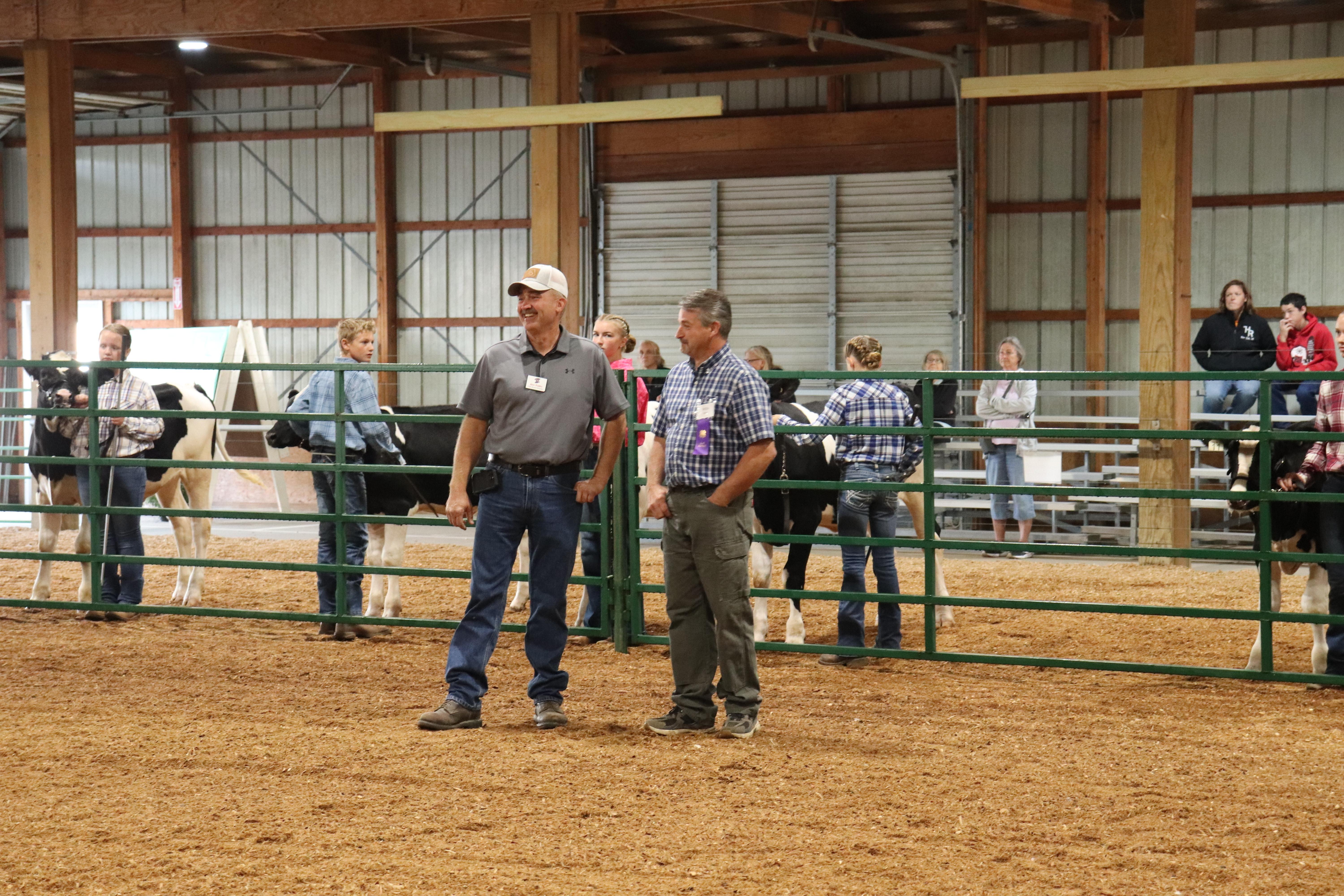 Two men talking in the middle of the arena with kids and dairy calves in the background.